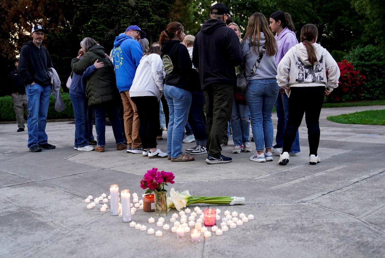 Mourners embrace near candles placed on ground.
